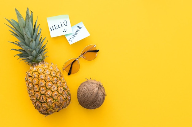 Ananas créatif regardant avec des lunettes de soleil bouteille de crème et de noix de coco isolée sur jaune