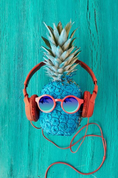 Ananas drôle peint en bleu en rouge dans des lunettes de soleil et des écouteurs