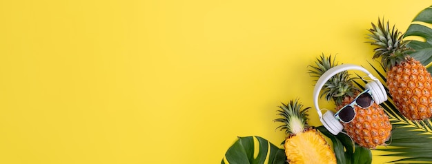 Ananas drôle portant un casque blanc écouter de la musique isolée sur fond jaune avec des feuilles de palmier tropical vue de dessus concept de design plat