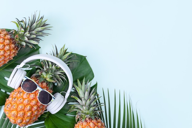 Ananas drôle portant des écouteurs blancs et des lunettes de soleil sur les feuilles