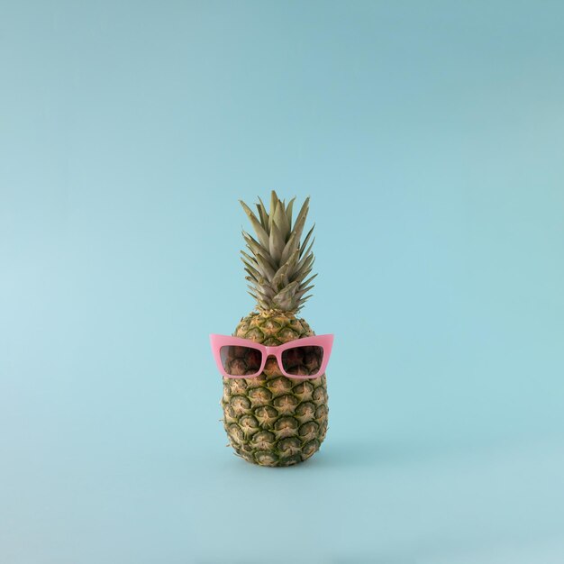 Ananas frais de fond d'été avec des lunettes de soleil roses sur fond bleu