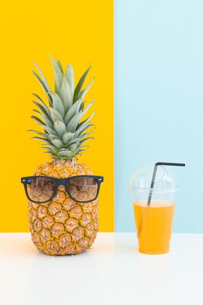 Ananas frais avec des lunettes de soleil près d'un verre de jus et d'une paille à cocktail sur fond de couleur