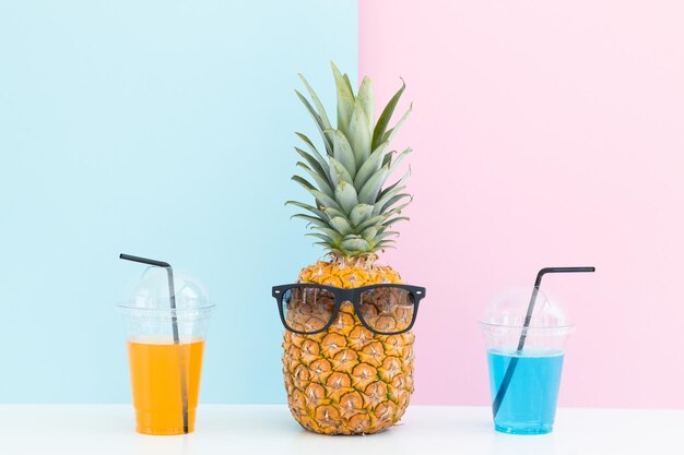 Ananas frais avec des lunettes de soleil près d'un verre de jus et d'une paille à cocktail sur fond de couleur