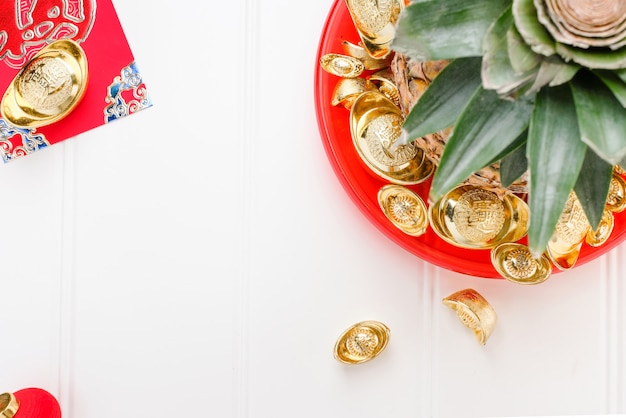 Ananas avec groupe de lingots d&#39;or dans un plateau rouge sur une table en bois blanc