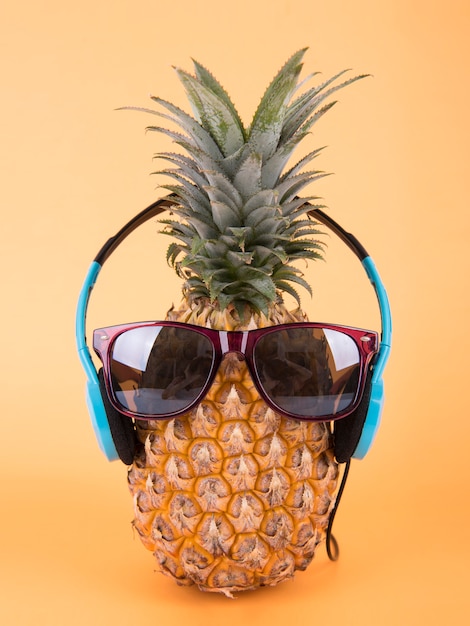 Ananas avec des lunettes de soleil et un casque sur fond orange. concept d&#39;été de fruits.