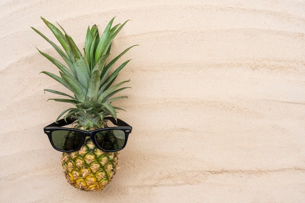 Ananas avec des lunettes de soleil sur la plage de sable pour une utilisation en toile de fond des vacances d'été