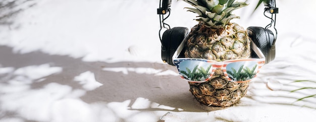 Ananas mûr juteux frais dans des lunettes de soleil sur le sable sous le soleil brûlant