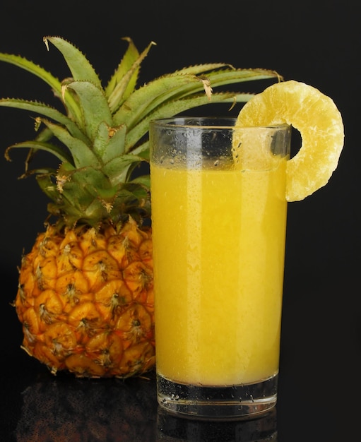 Ananas mûr et verre de jus isolé sur noir