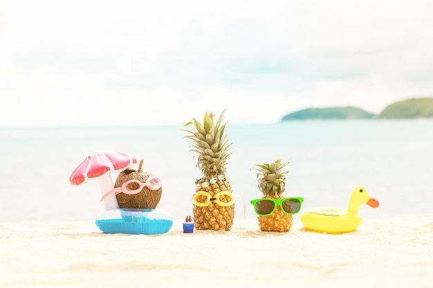 Ananas et noix de coco attrayants drôles dans des lunettes de soleil élégantes sur le sable contre la mer turquoise