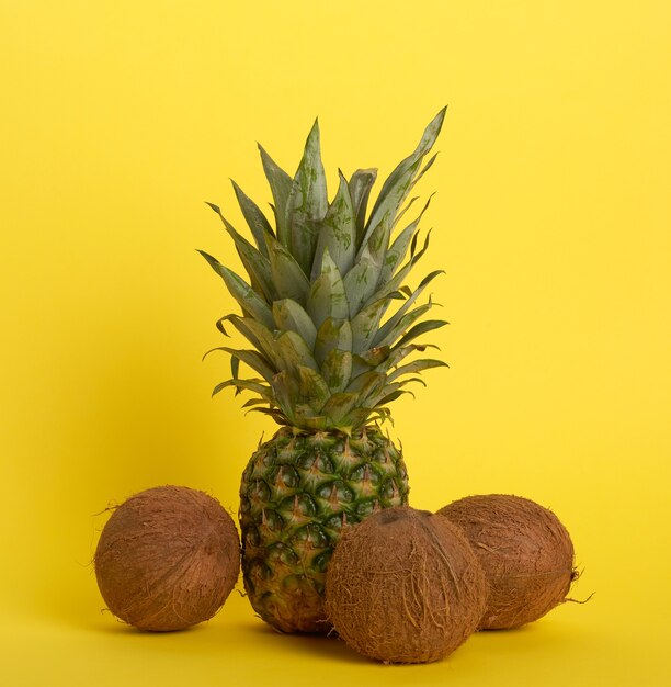 Ananas et noix de coco brunes entières sur un jaune