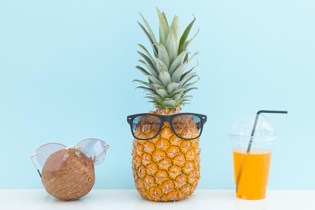 Photo ananas et noix de coco avec des lunettes de soleil se reposant et buvant un cocktail sur la plage vacances d'été