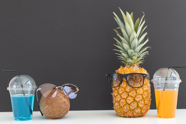 Ananas et noix de coco avec des lunettes de soleil se reposant et buvant un cocktail sur la plage Vacances d'été