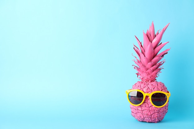 Ananas rose peint avec des lunettes de soleil sur fond bleu