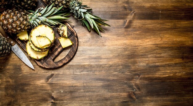 Ananas en tranches sur une planche à découper avec un couteau. Sur une table en bois.