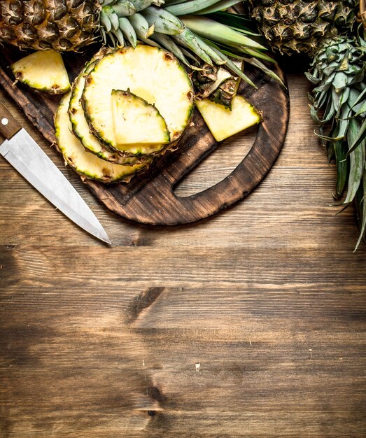 Ananas en tranches sur une planche à découper avec un couteau sur une table en bois.