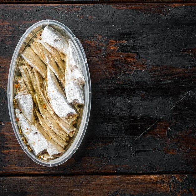 Anchois poisson en conserve dans une boîte de conserve fruits de mer dans un récipient en plastique sur une vieille table en bois sombre backgroundxA vue de dessus à plat avec espace pour copie et espace pour le format carré du texte