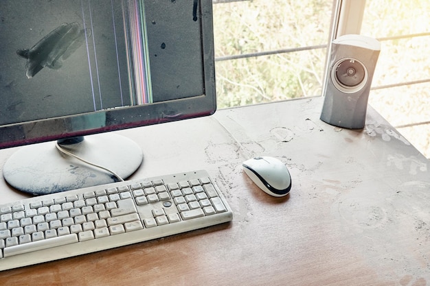 L'ancien clavier avec souris et moniteur cassé avec haut-parleur audio sont sur une table en bois et recouverts d'une épaisse poussière dans un atelier