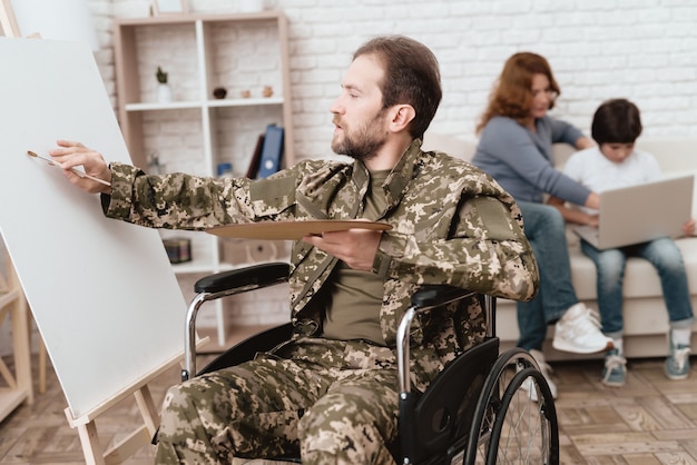 Un ancien combattant en fauteuil roulant a la peinture et un pinceau dans les mains.