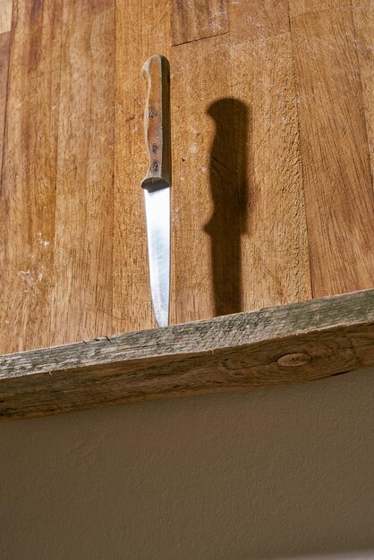 Ancien couteau à fruits avec manche en bois poignardé sur une étagère de cuisine en bois.