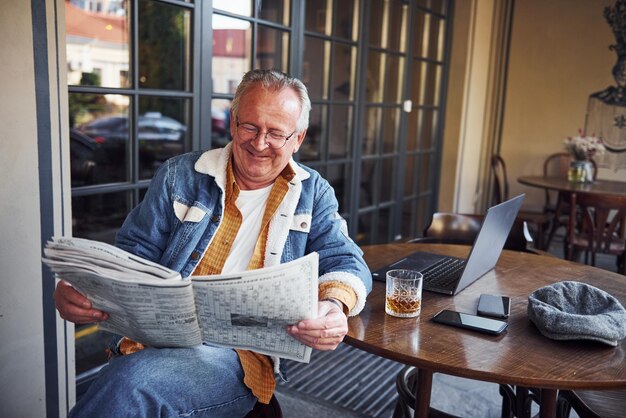 Photo un ancien élégant en vêtements à la mode et en lunettes est assis dans le café et lit le journal.