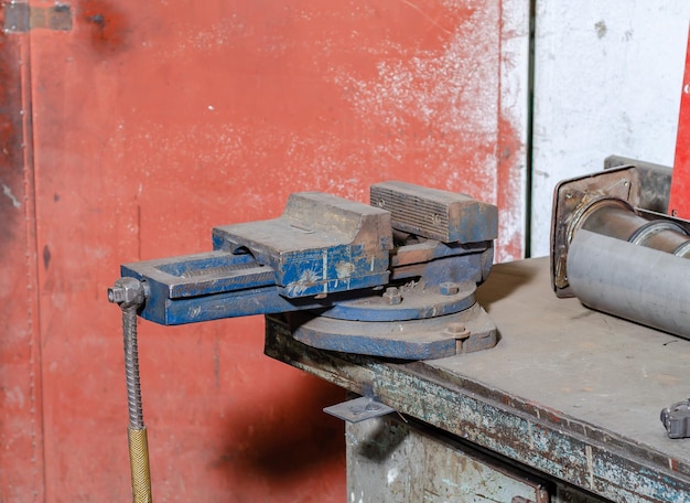Ancien étau en fer bleu sur un atelier d'établi dans un environnement flou d'autres équipements et outils une pince spéciale pour les pièces