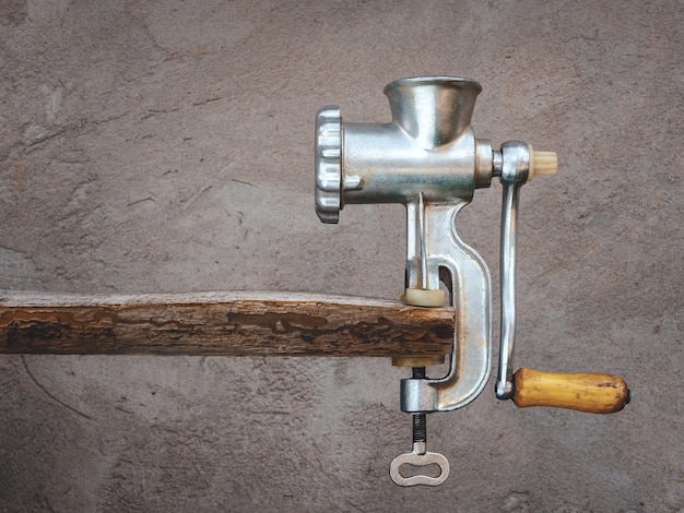 Ancien hachoir à viande sur une planche de bois sur un fond d'un mur de béton