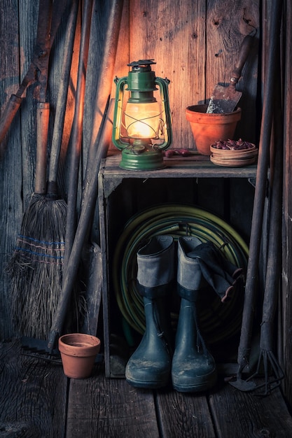 Un ancien hangar rustique avec outils de jardin et lampe à huile