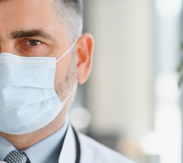 Ancien médecin professionnel de la santé mature portant des lunettes de stéthoscope à blouse blanche et un masque facial debout à l'hôpital Concept de protection des soins de santé du personnel médical Portrait