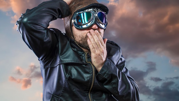 Ancien pilote d'avion sur fond de nuages d'orage avec visage expressif. lunettes et vieux chapeau avec veste en cuir noir