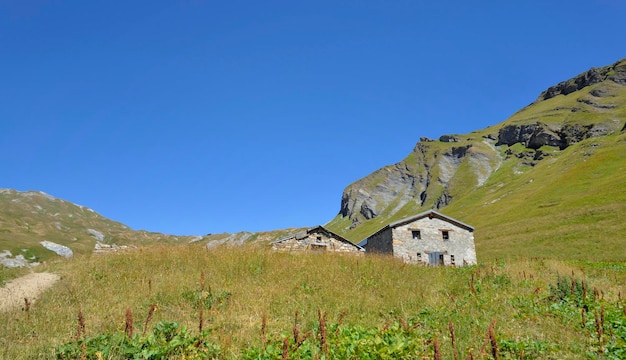 Ancienne bergerie dans les prés avec montagne alpine en arrière-plan sous ciel bleu