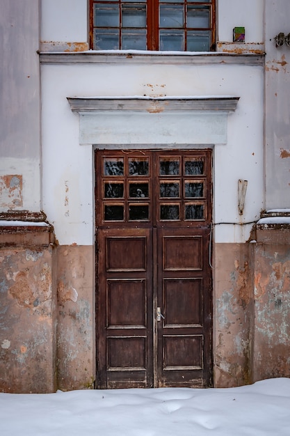 Ancienne entrée de l'immeuble. Mur blanc. Porte en bois. Jour de neige.