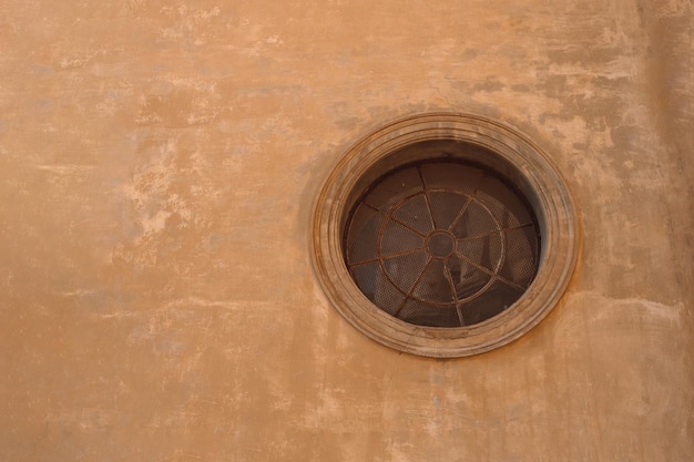 Ancienne fenêtre ronde ancienne avec treillis de fer encadrée sur un mur de brique beige en Europe