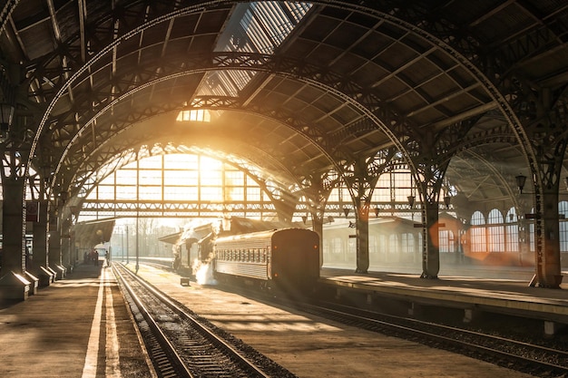 Ancienne gare ferroviaire avec un train et une locomotive sur la plate-forme en attente de départ Rayons de soleil du soir dans les arcs de fumée