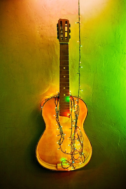 Ancienne guitare cassée décorée de guirlande lumineuse sur le mur. Décoration intérieure de Noël. Ampoules du Nouvel An