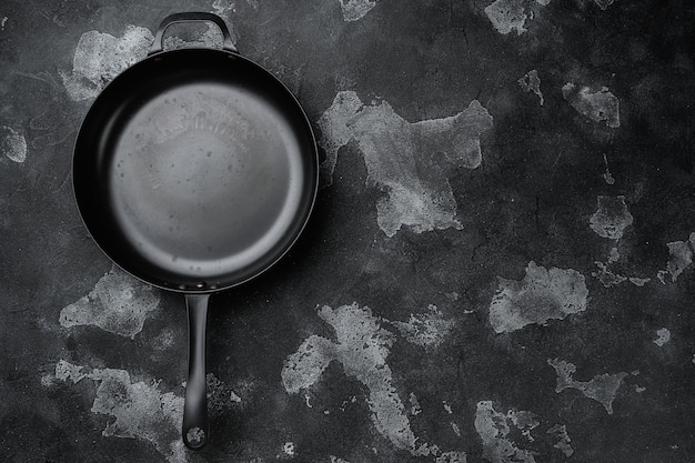 Ancienne poêle à frire vide utilisée avec espace de copie pour le texte ou la nourriture avec espace de copie pour le texte ou la nourriture, vue de dessus à plat, sur fond de table en pierre noire noire