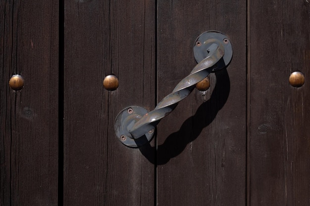 Ancienne poignée de porte en fer torsadé sur porte en bois. Fragment d'une clôture en planches de bois avec rivets métalliques. fermer