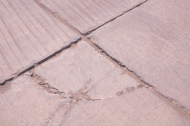 L'ancienne rue en béton brisée endommagée avec des lignes de fissures effondrées et grandes sur la surface