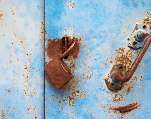 Ancienne serrure rouillée accrochée à une porte en métal bleu