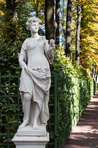 Ancienne statue de parc d'une femme sensuelle de l'époque de la Renaissance grecque ou italienne avec des fleurs dans le parc de la ville est allée aux couleurs dorées de l'automne,