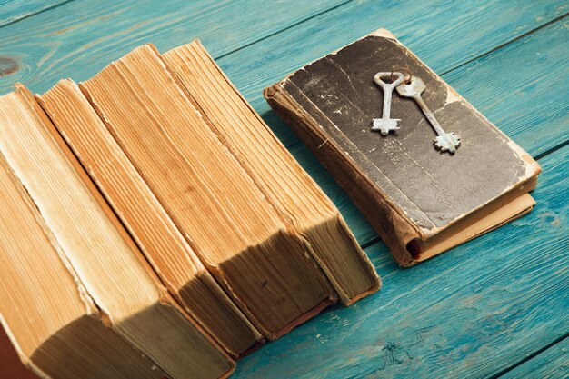 Anciennes clés sur un vieux livre et pile de livres anciens sur fond de bois bleu