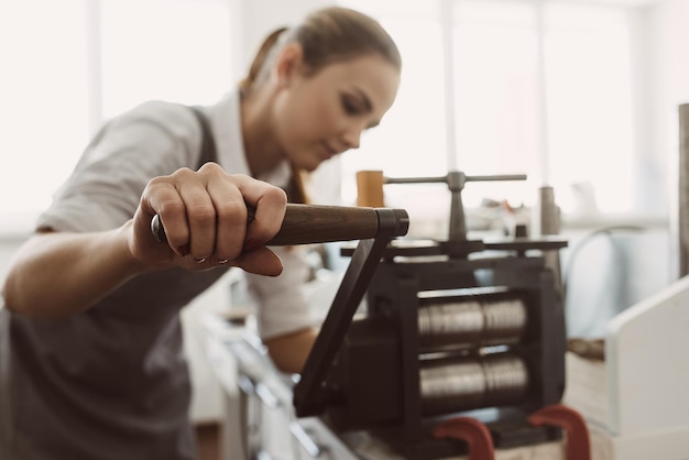 Anciennes technologies jeune femme orfèvre artisanat métal sur machine à rouler en atelier