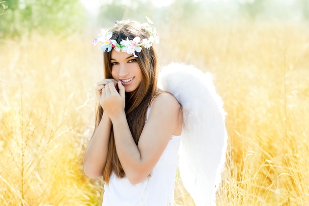 Ange fille dans un champ doré avec des ailes de plumes blanches