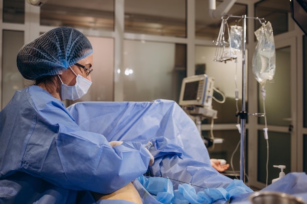 Un angiochirurgien expérimenté opère sur la jambe d'un patient avec des varices Un médecin dans un masque de protection et une blouse d'opération se concentre sur l'opération sur la jambe du patient