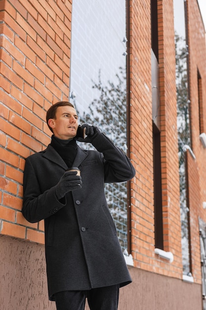 Angle bas d'un homme d'affaires adulte avec une tasse de café en papier pour passer un appel téléphonique près d'un immeuble de bureaux