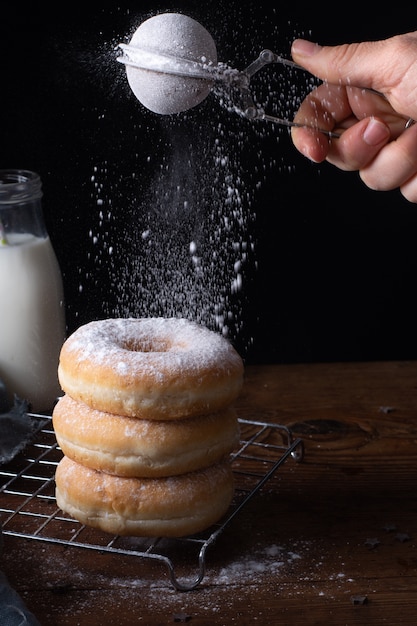 Angle élevé de beignets empilés avec glaçage à la main avec du sucre en poudre