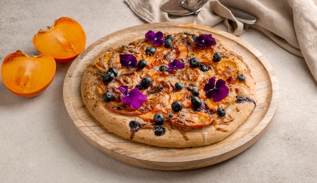 Angle élevé de délicieuses pizzas cuites avec des kakis et des pétales de fleurs