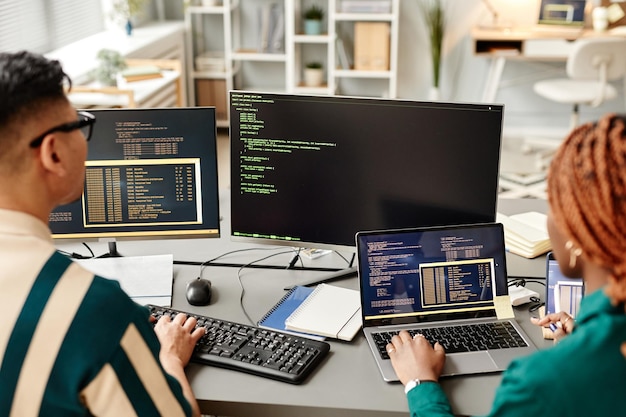 Angle élevé de deux développeurs informatiques utilisant des ordinateurs lors de l'examen du code au bureau