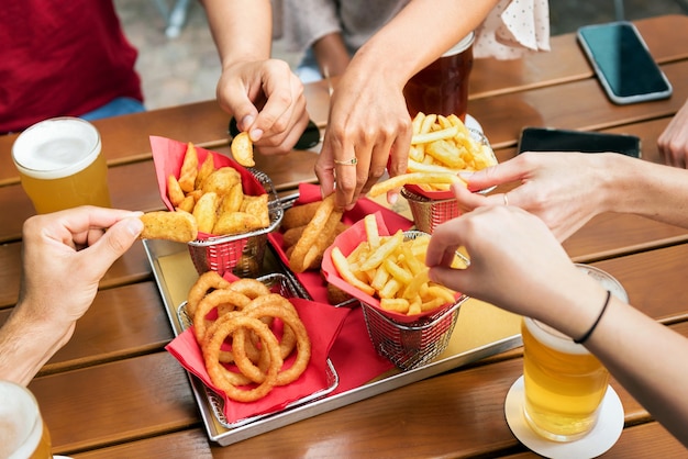 Angle élevé d'un groupe d'amis méconnaissables de la récolte prenant des frites et des rondelles d'oignon croustillantes du plateau tout en se réunissant et en buvant de la bière au pub