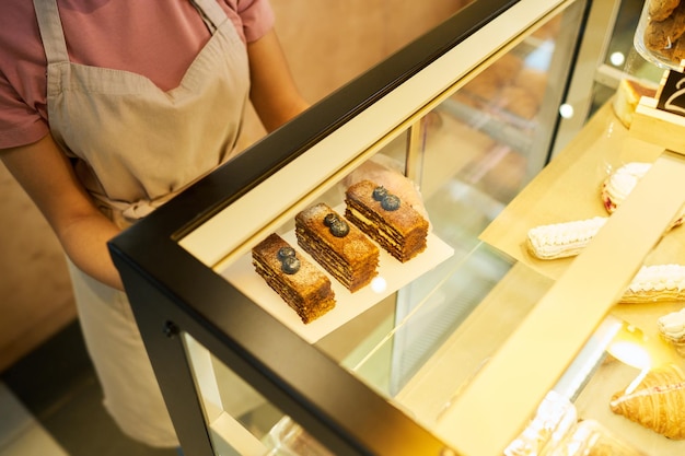 Angle élevé de jeune commis de boulangerie mettant des gâteaux en exposition