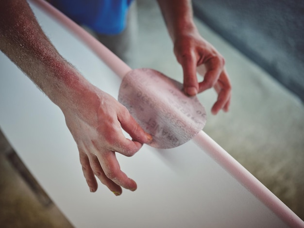 Angle élevé de récolte artisan anonyme avec des tatouages façonner et poncer une planche de surf en bois dans l'atelier